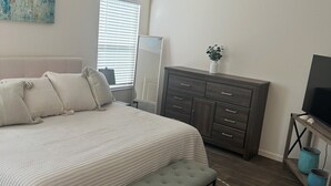 A bedroom with a bed, a bench, a dresser, a TV, and a ceiling fan. - Centrally Located close to Brownwood, Sawgrass and Eastport with Golf Cart. (The Villages)
