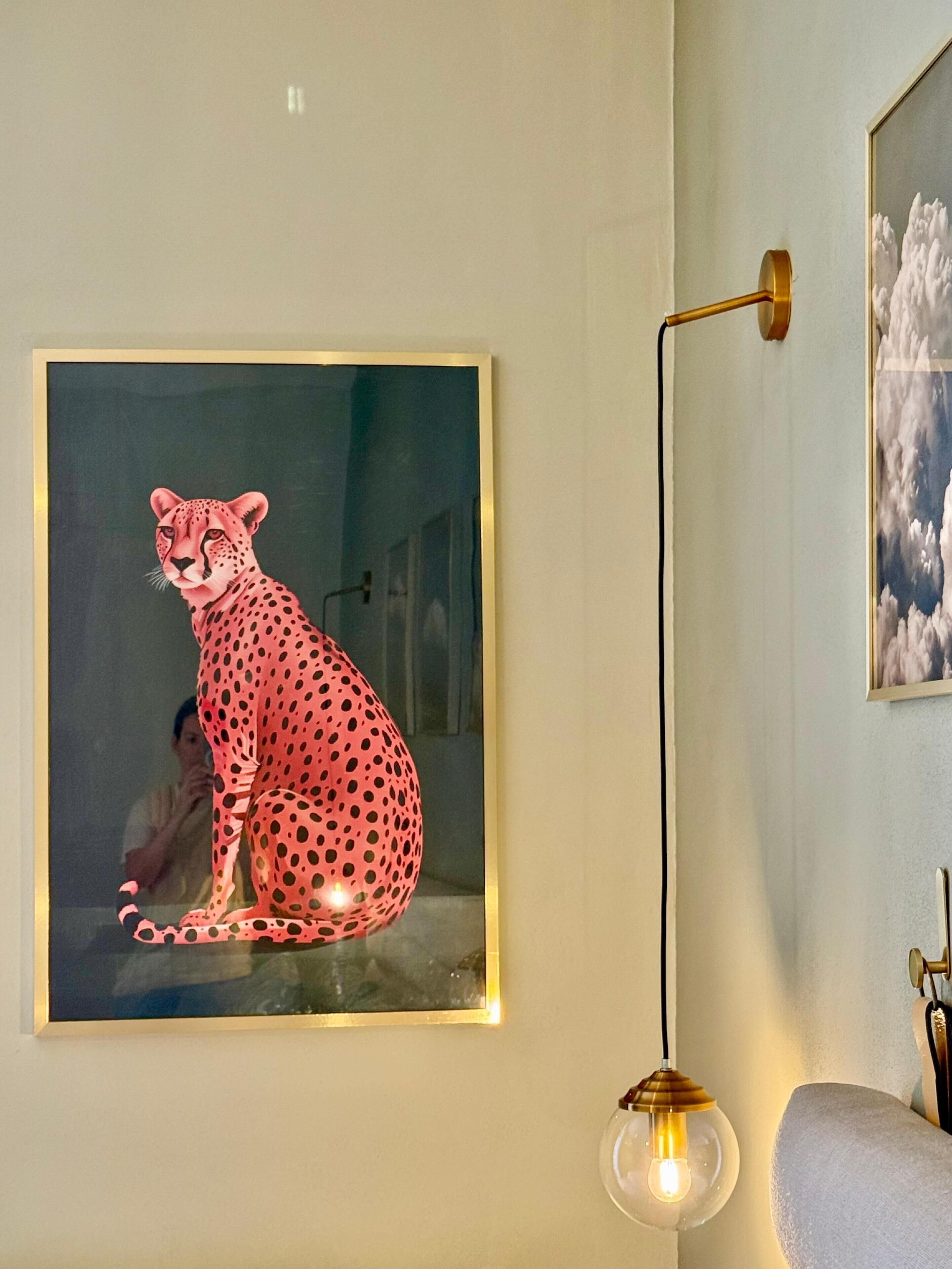 A framed artwork of a cheetah on a wall, a floor lamp, and a partial view of a couch.