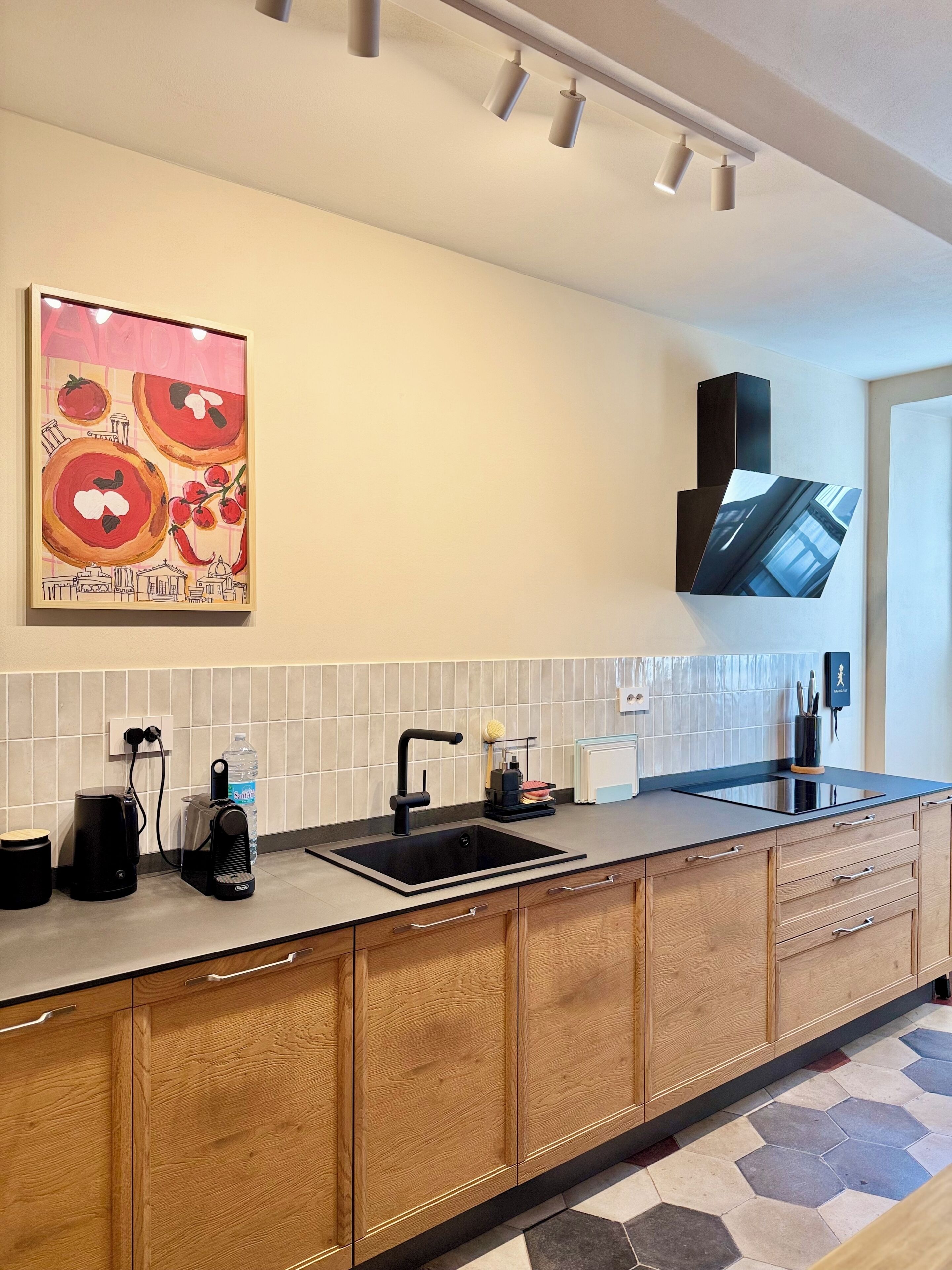 A modern kitchen with a black sink, wooden cabinets, a tiled backsplash, and a mounted flat-screen TV.