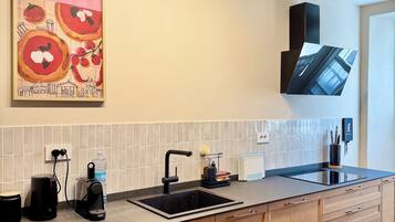 A modern kitchen with a black sink, wooden cabinets, a tiled backsplash, and a mounted flat-screen TV.