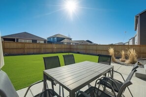 A backyard with a wooden fence, a lawn, and a patio area with a table and chairs. - New Spacious and Luxurious Home (Colorado Springs)
