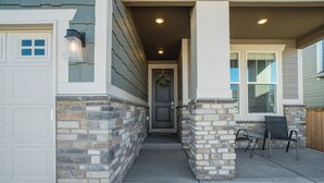 A house with a stone exterior, a front door, and a covered porch with two chairs. - New Spacious and Luxurious Home (Colorado Springs)