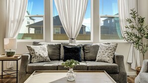 A living room with a grey sofa, patterned cushions, a vase with green plants, and a wooden coffee table. - New Spacious and Luxurious Home (Colorado Springs)