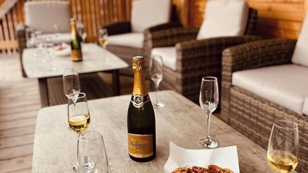 Une table avec une bouteille de champagne, des verres et une assiette de nourriture, le tout disposé dans un cadre extérieur agréable, avec des meubles en osier.