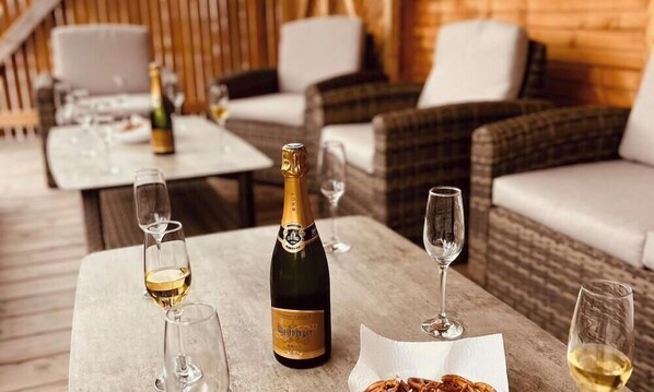 A table with a bottle of champagne, glasses, and a plate of food in a cozy outdoor setting with wicker furniture. - Le Noisetier near EUROPAPARK, RULANTICA (30minutes away) Christmas market in Alsace (Sundhouse)