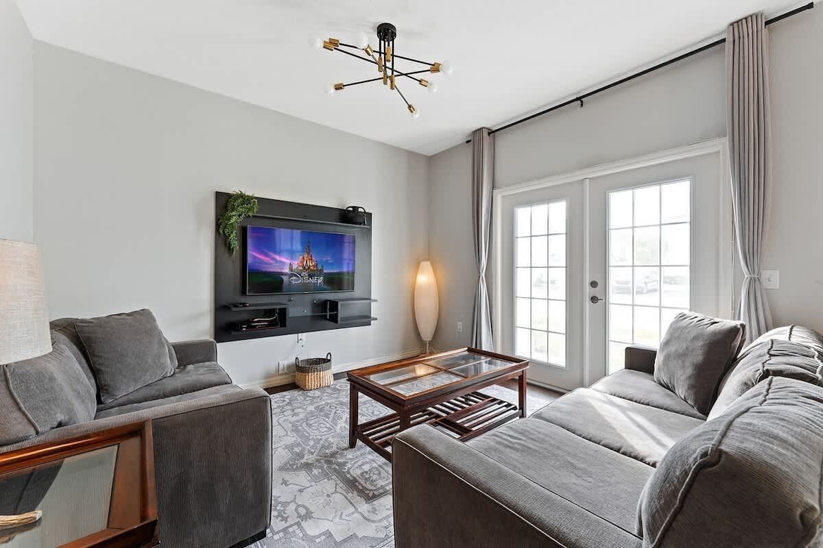 Ett modernt vardagsrum med en grå soffa, ett soffbord, en tv som är monterad på väggen och ett stort fönster med gardiner.