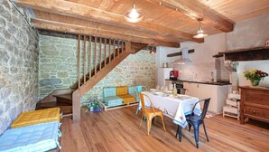 A rustic interior with a stone wall, wooden staircase, a sofa, a dining table with chairs, and a kitchen area. - Tuscan Organic Farm House Alba Etrusca (cortona)