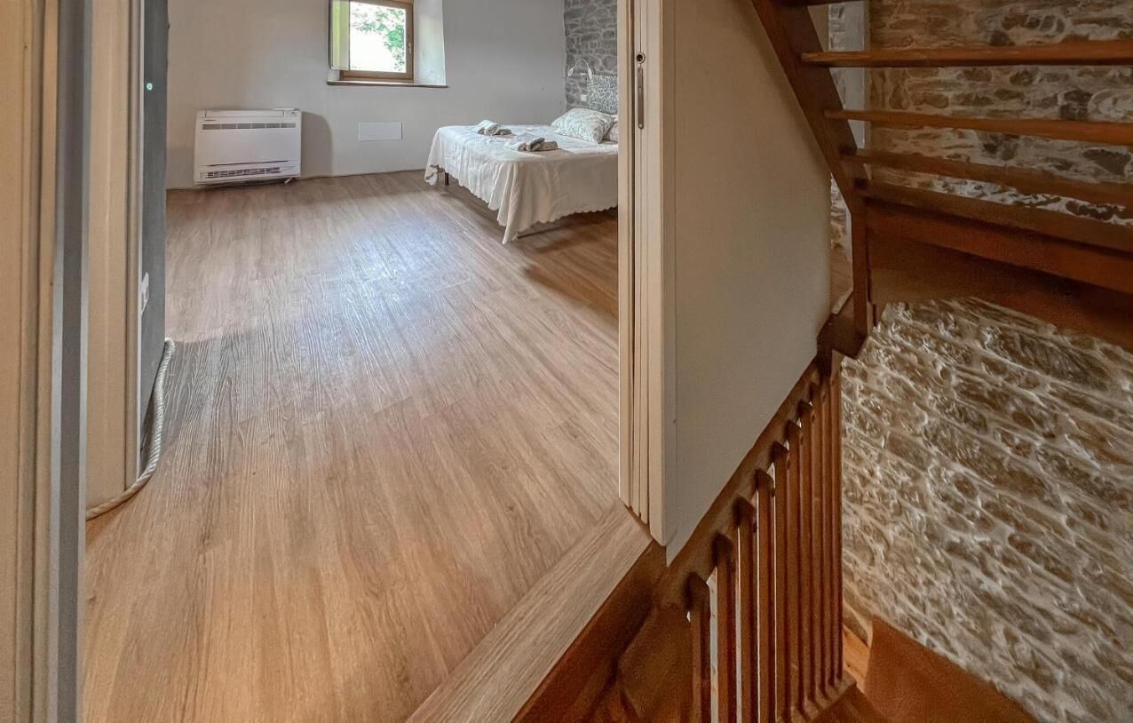 Een kamer met een houten vloer, een bed met wit beddengoed, een raam en een stenen muur.