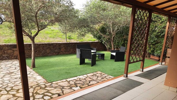 Een terras met kunstgras, stenen vloer en tuinmeubilair.