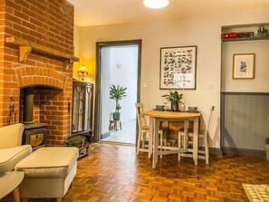 A cozy living room with a brick fireplace, a dining table with chairs, and a potted plant.