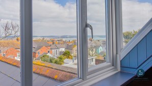 Une vue depuis une fenêtre donnant sur une ville côtière, avec des maisons et une étendue d’eau.