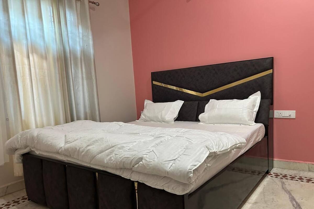 A bed with a dark headboard and white bedding in a room with pink walls and a patterned floor.