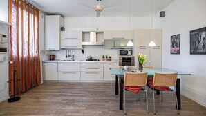 Una cocina moderna con armarios blancos, una mesa de comedor de vidrio, sillas de mimbre y un ventilador de techo.