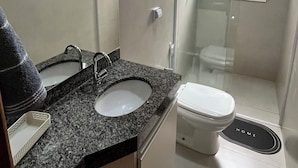 Een moderne badkamer met een wastafelblad van graniet, een toilet en een douche met glazen wanden.