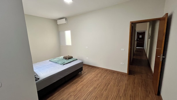 Een kleine, schone kamer met een enkel bed, een raam en een deur naar een andere kamer.