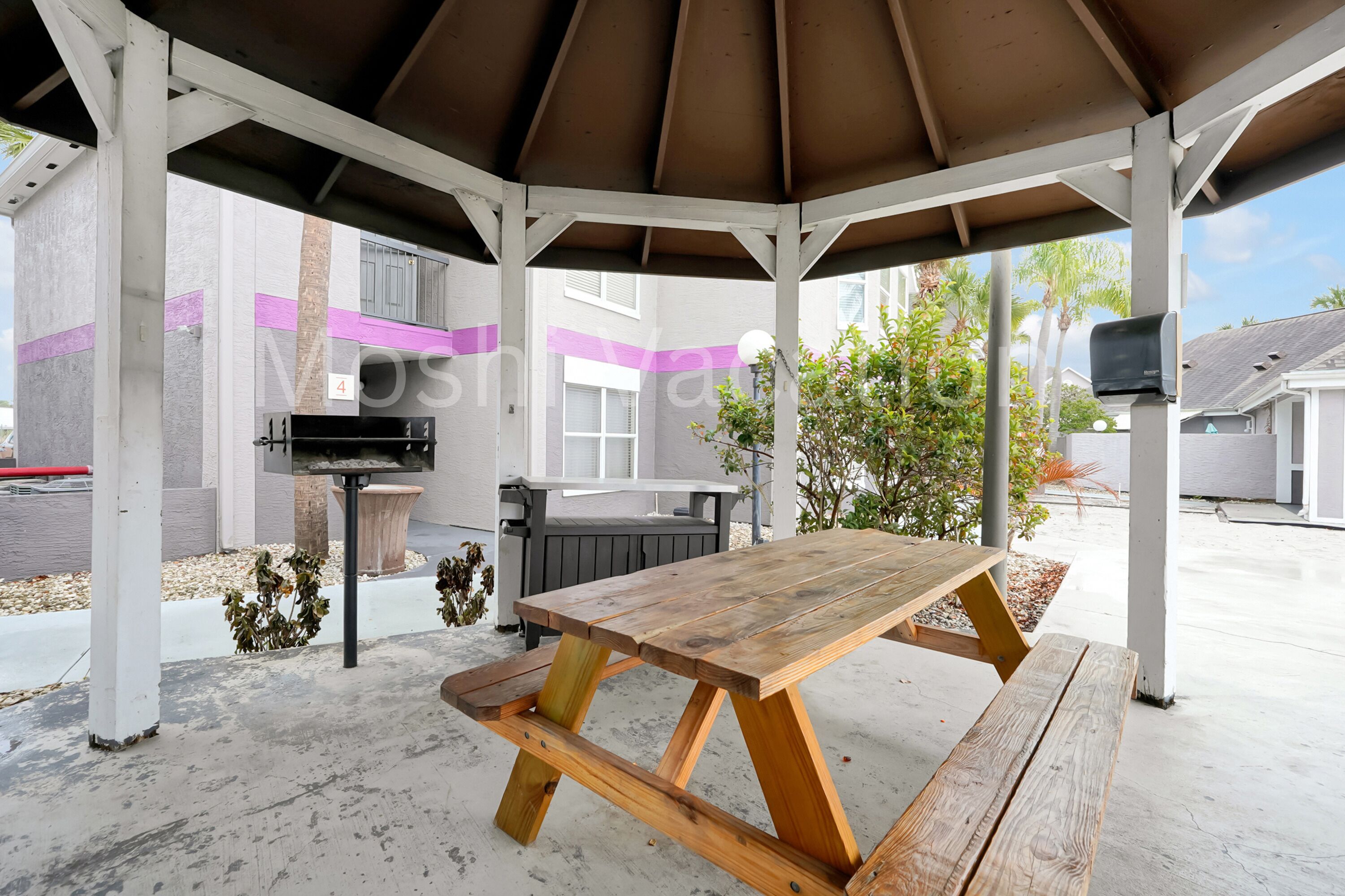 A covered outdoor area with a wooden picnic table and a barbecue grill.