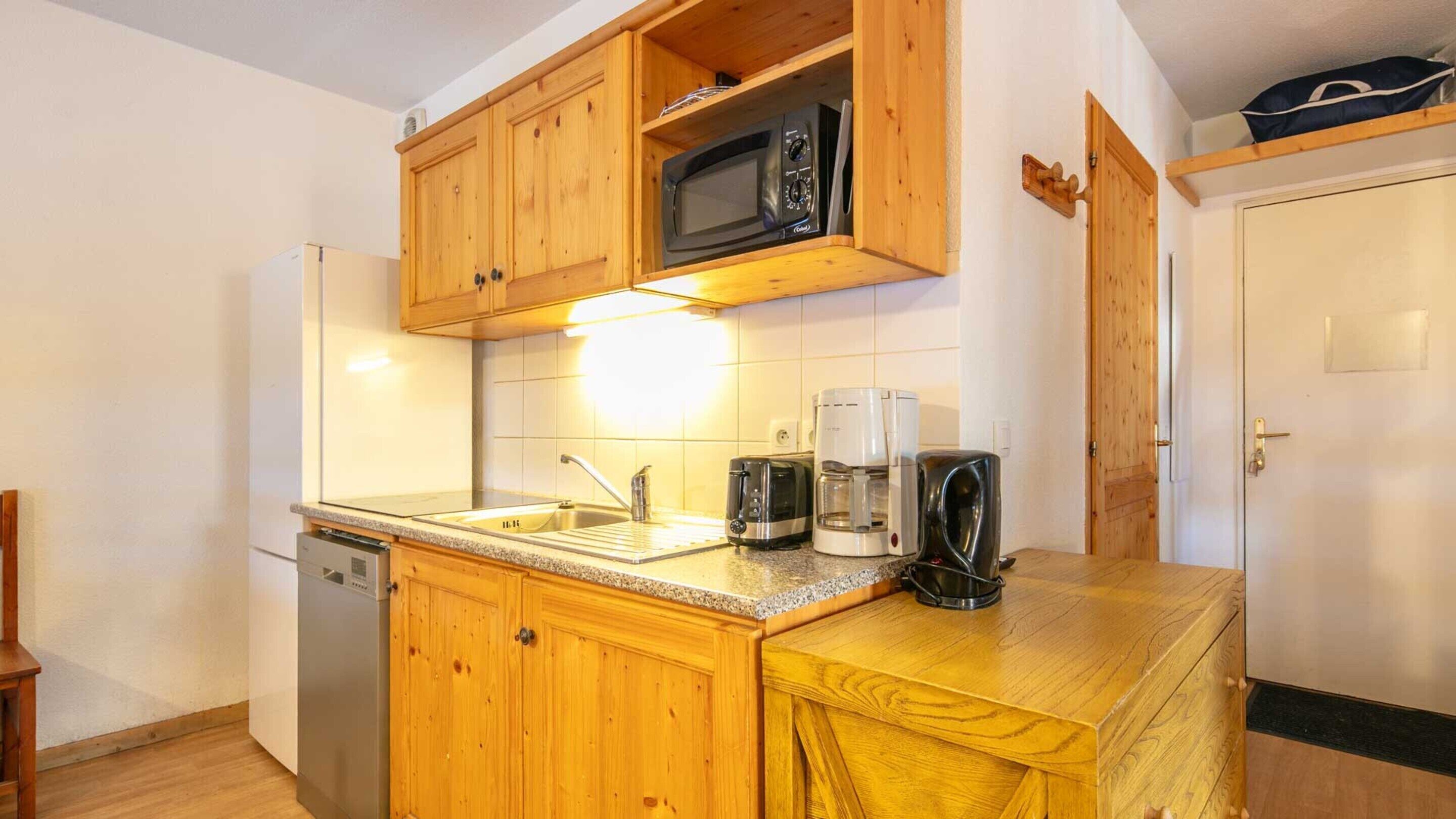 A compact kitchen with wooden cabinets, a microwave, a toaster, and a coffee maker.