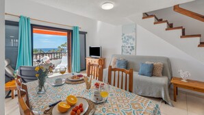 A dining area with a table set for breakfast, a sofa, a TV, and a staircase. - Vacation Home 'Santiago Beach' with Sea View, Shared Pool and Wi-Fi (Costa Adeje)