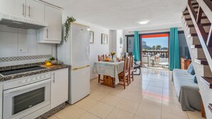 A compact kitchen with a stove, oven, and white cabinets. There's a dining area with a table and chairs, and a balcony with a view. - Vacation Home 'Santiago Beach' with Sea View, Shared Pool and Wi-Fi (Costa Adeje)
