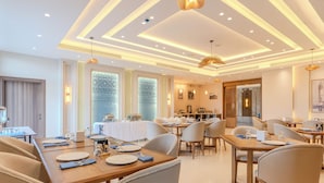 Un espace de restauration moderne, doté de plusieurs tables et chaises, d’un plafond pourvu d’un éclairage linéaire et d’une grande fenêtre avec du verre décoratif.