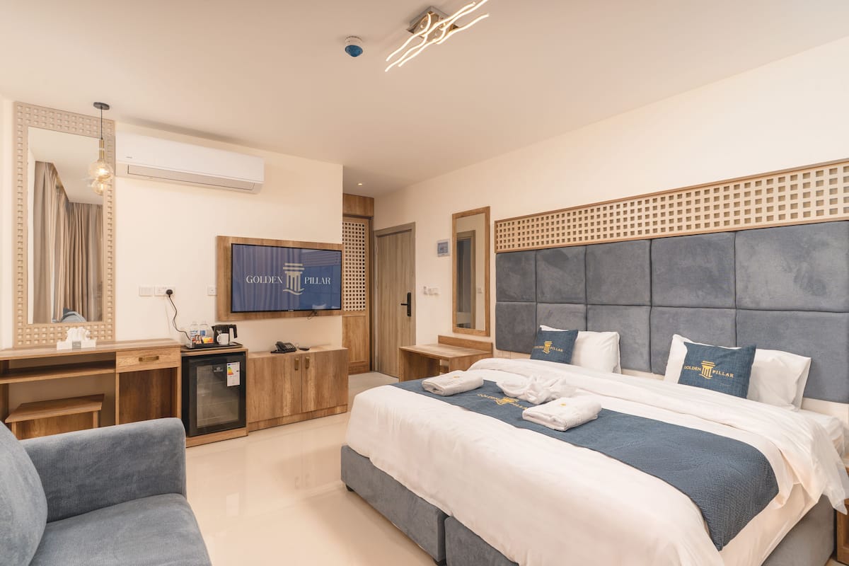 A modern hotel room with a large bed, a desk, a television, and a minibar.