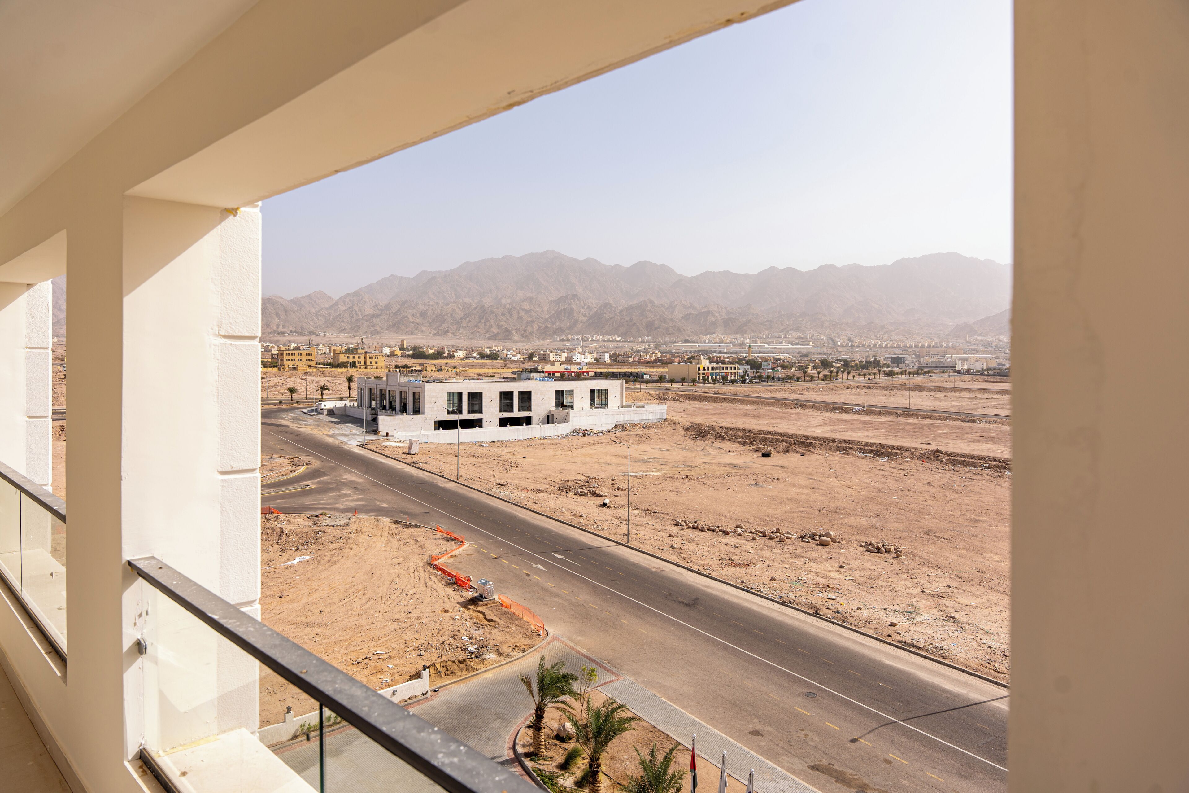 A view from a balcony overlooking a road with a building in the distance and mountains in the background.