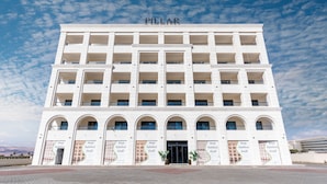 Un immeuble à plusieurs étages, sur lequel on peut lire le nom « PILLAR » en haut. Il présente une façade symétrique, avec de nombreux balcons et des fenêtres en arc de cercle.