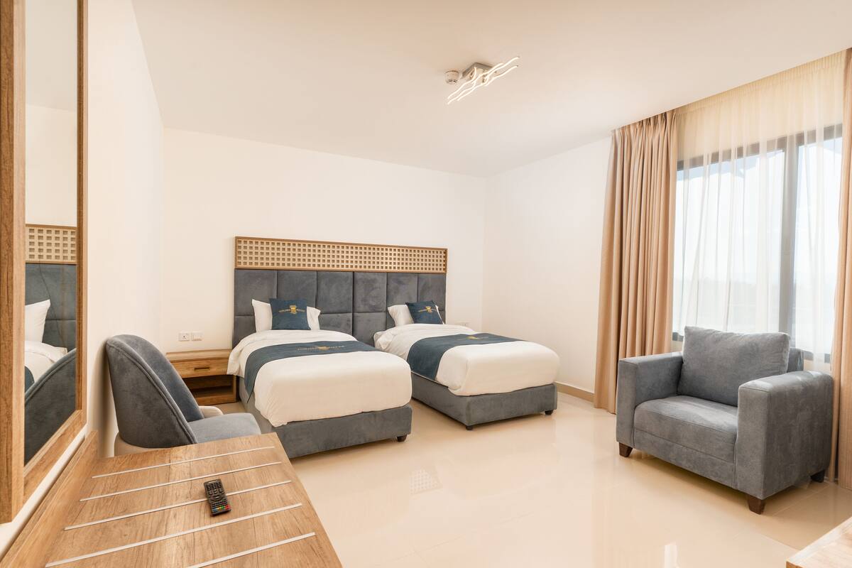 A hotel room with two beds, a sofa, a wooden desk, and a mirror.