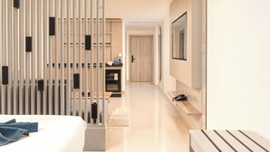 Une chambre d’hôtel moderne équipée d’un lit, d’un téléviseur fixé au mur, d’un bureau avec une chaise et d’une porte coulissante avec des stores verticaux.