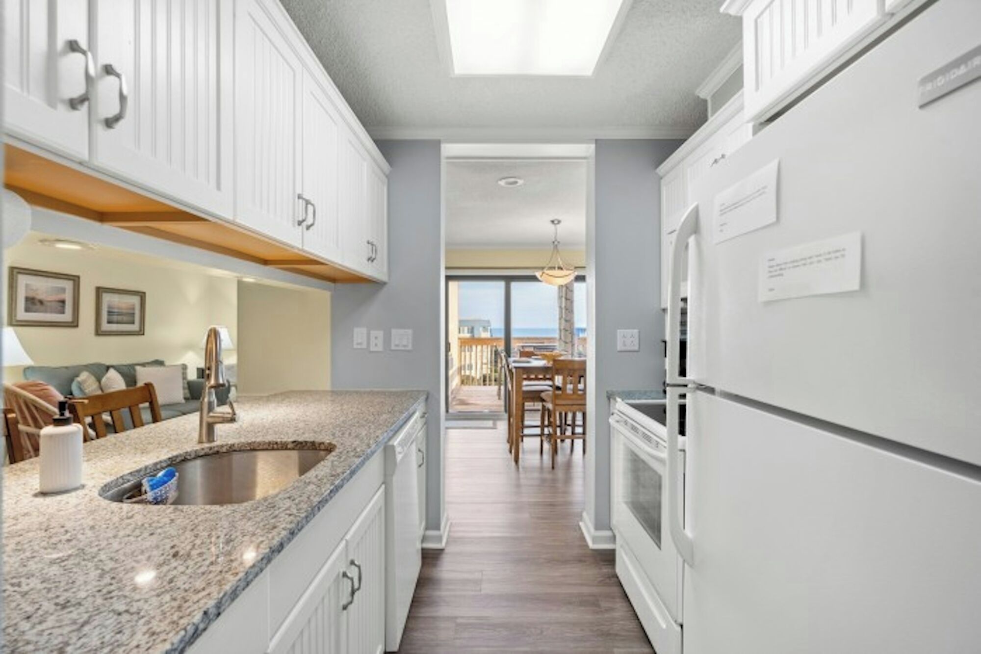 A modern kitchen with white cabinetry, granite countertops, and a view to a dining area.