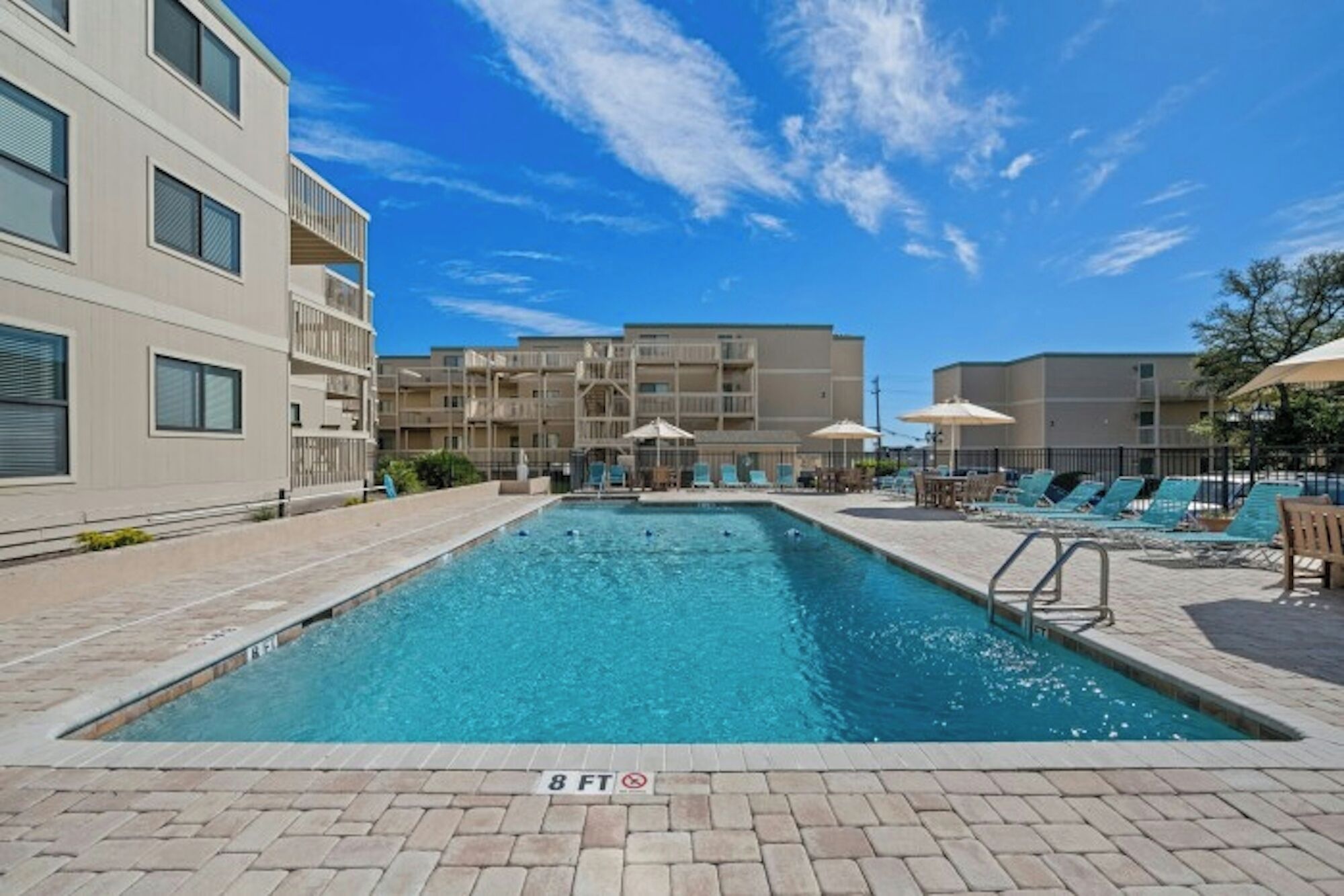 A swimming pool with a 8 FT depth marker, surrounded by lounge chairs and umbrellas, with a clear blue sky above.