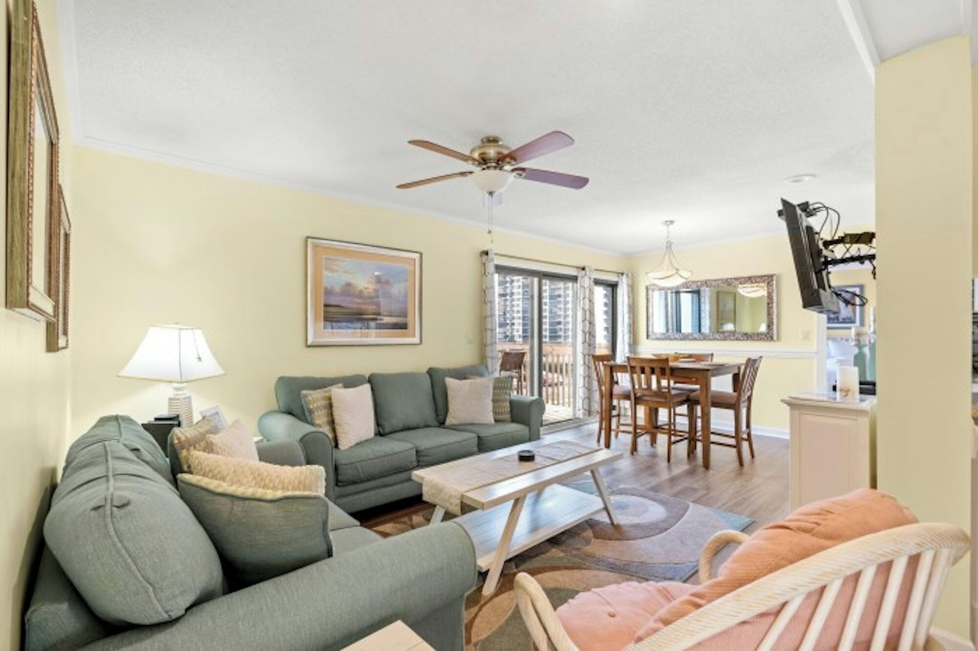 A living room with a sofa, a coffee table, a ceiling fan, and a dining area with a table and chairs.