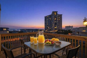 A balcony with a table set for two, featuring a pitcher of orange juice, glasses, a bowl of fruit, and a bowl of nuts. - Ocean Bridge Building 1 Unit C2 - Ocean View (Myrtle Beach)