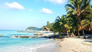 Ein Strand mit klarem türkisblauem Wasser, Palmen und einer umbauten Hütte.