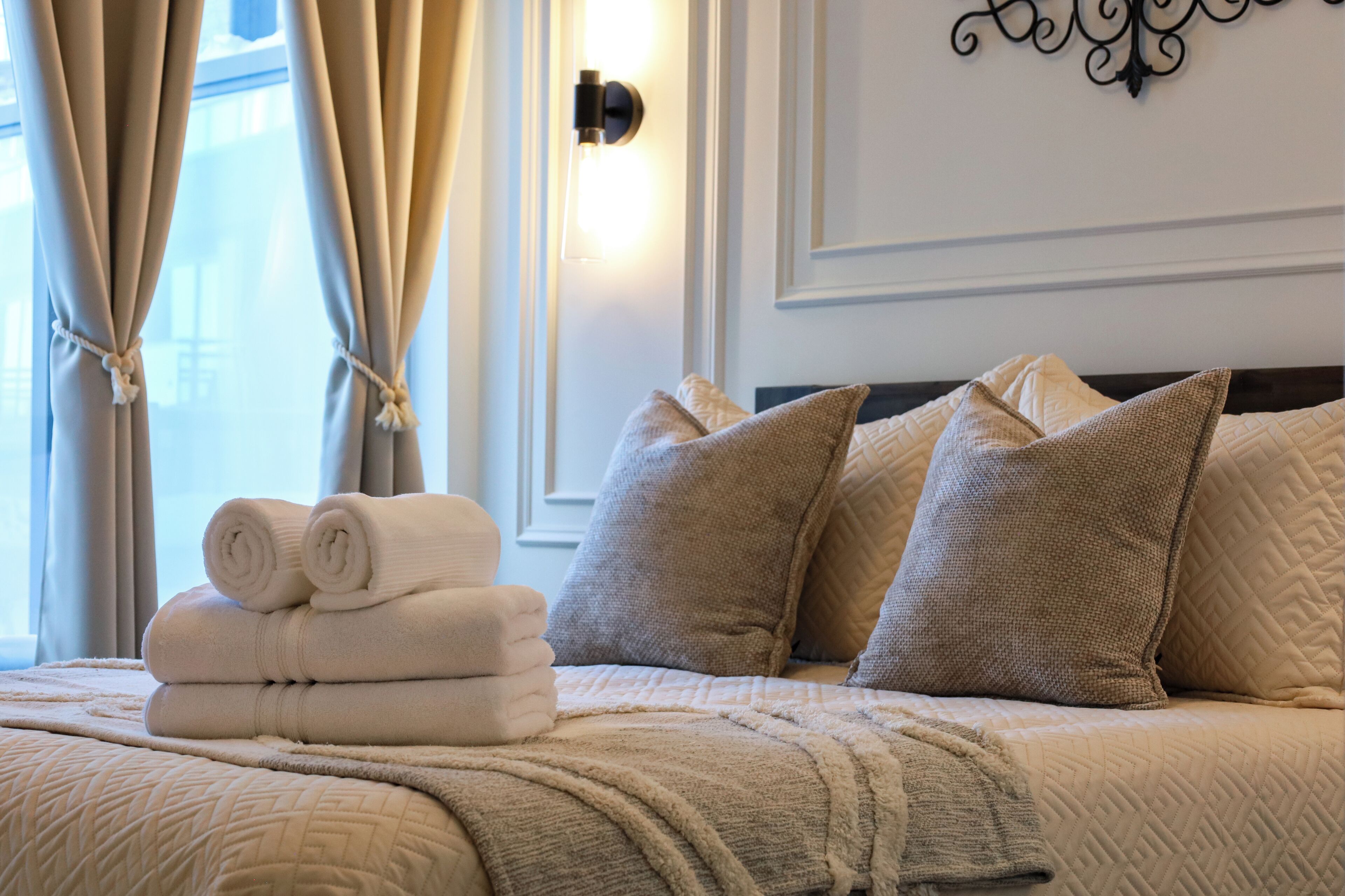 Un letto rifatto con cura, asciugamani bianchi arrotolati, cuscini color beige e una coperta trapuntata.