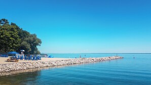 Una playa con agua cristalina, un rompeolas rocoso y sillas y sombrillas azules.