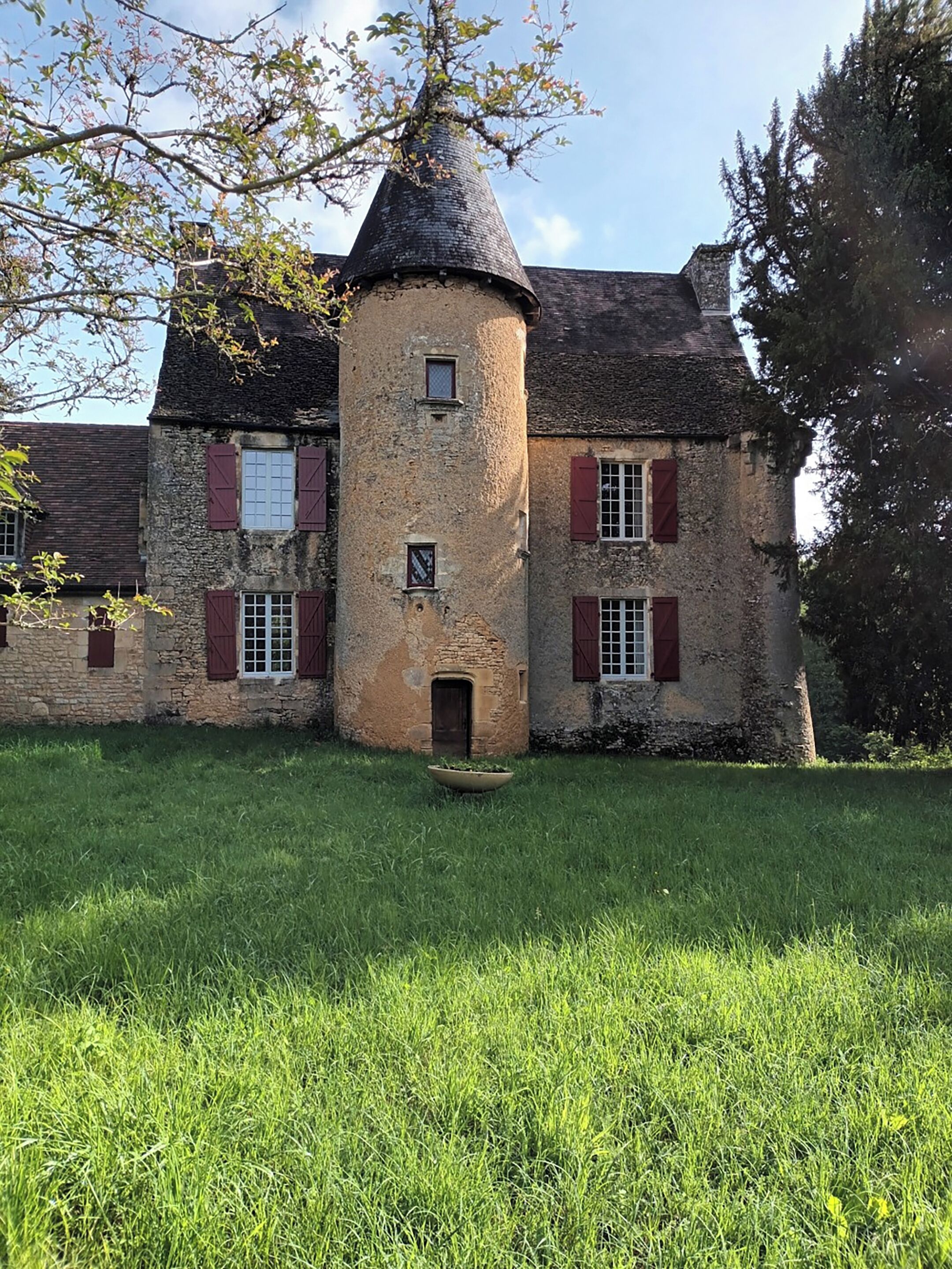 A stone building with a turret, red shutters, and a grassy courtyard.