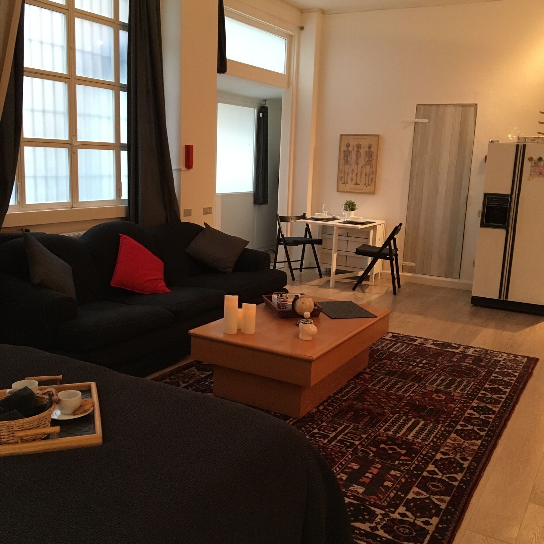 Ein modernes Wohnzimmer mit einem dunkelgrauen Sofa, einem Couchtisch mit Kerzen und einer Essecke mit kleinem Tisch und Stühlen.