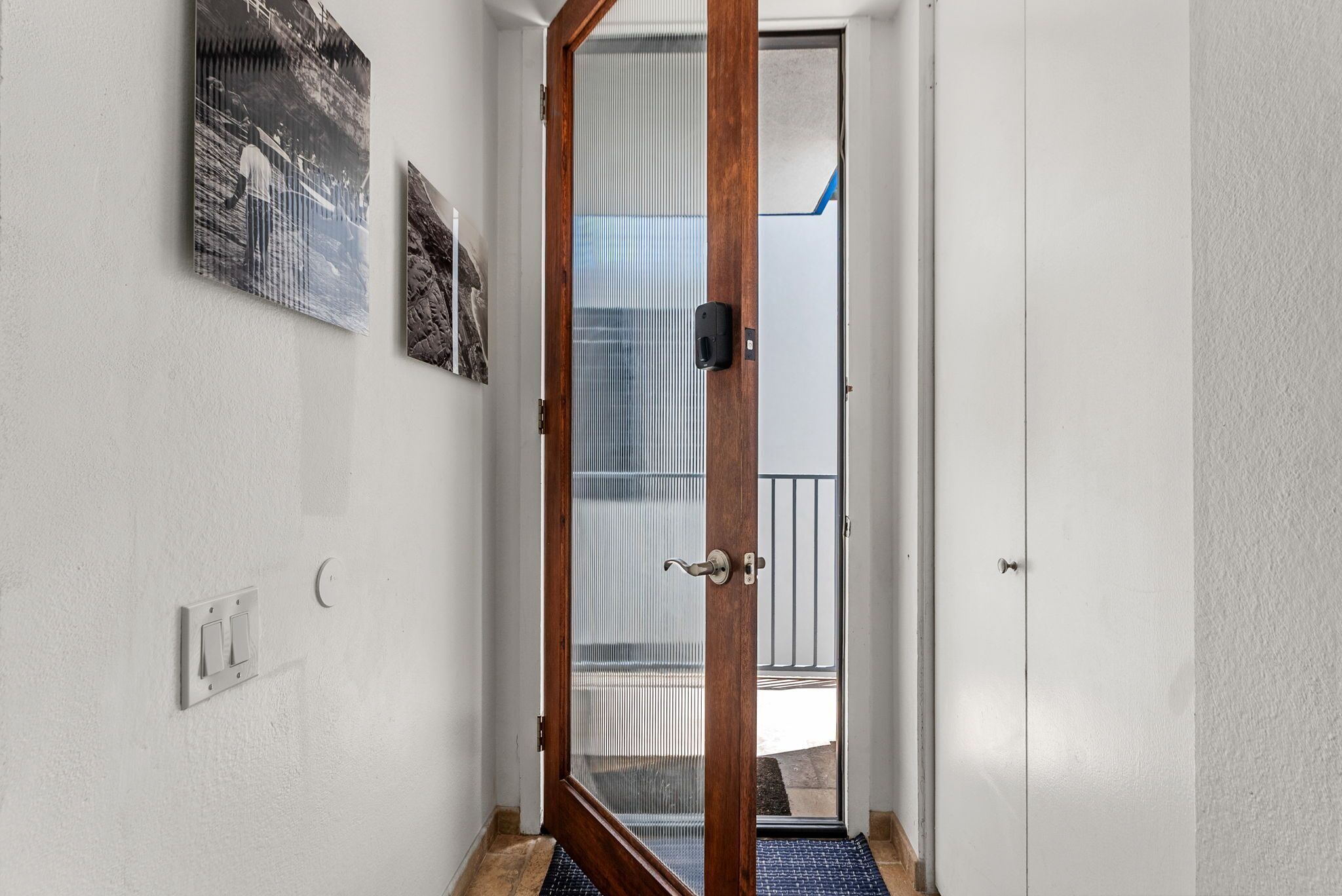 A hallway with a wooden door, a white wall, and a black mat at the entrance.