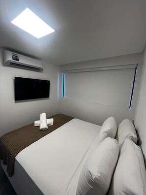 A hotel room with a bed, a flat-screen TV mounted on the wall, an air conditioning unit, and a window with blinds. - Marina do Cupe 203 (Ipojuca)