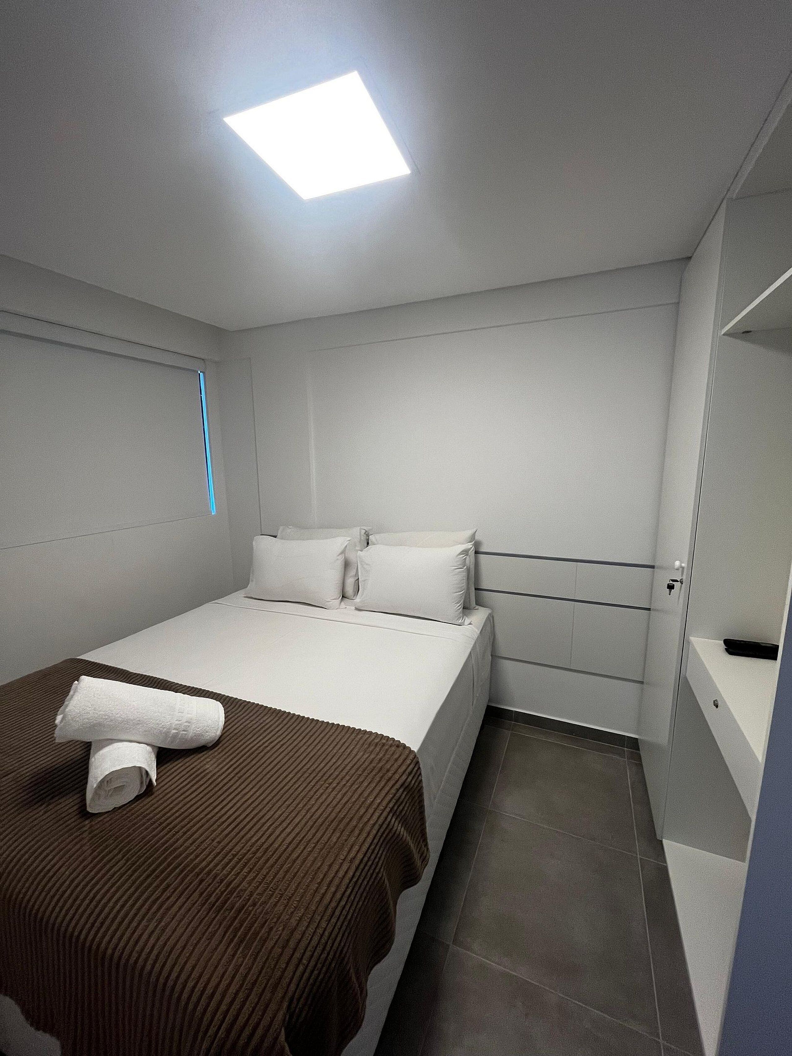 A modern hotel room with a large bed, a bedside table, a nightstand, and a built-in wardrobe.