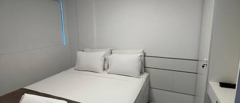A modern hotel room with a large bed, a bedside table, a nightstand, and a built-in wardrobe.