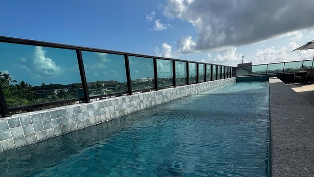 A rooftop infinity pool with a glass railing, offering a view of the cityscape and palm trees. - Marina do Cupe 203 (Ipojuca)