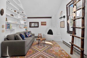 Una sala de estar con un sofá, un tapete estampado, una chimenea y una escalera.