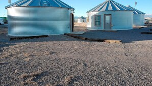 Two yurts with a corrugated metal exterior and a conical roof, situated on a gravel ground with a clear sky. - Grain Bin Studio Suite: Unique Stay in the SLV (Moffat)