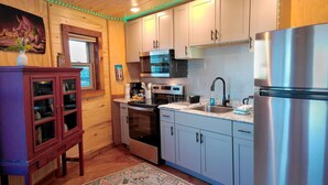 A compact kitchen with wooden cabinets, a stainless steel refrigerator, a microwave, and a stove. - Grain Bin Studio Suite: Unique Stay in the SLV (Moffat)