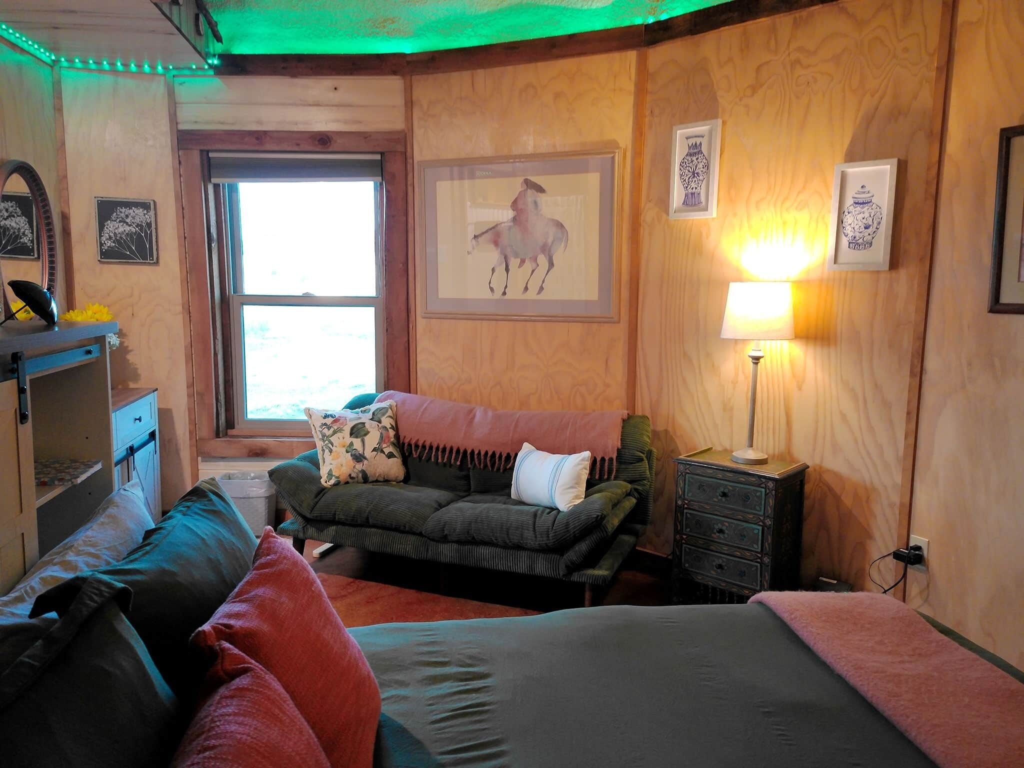 A cozy room with a sofa, a bed, and a dresser. There is a window with a view outside.
