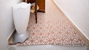 A narrow hallway with patterned floor tiles, a white trash bin, a wooden table with a bowl and plate, and a door at the end. - Casa Lucia  (Positano)