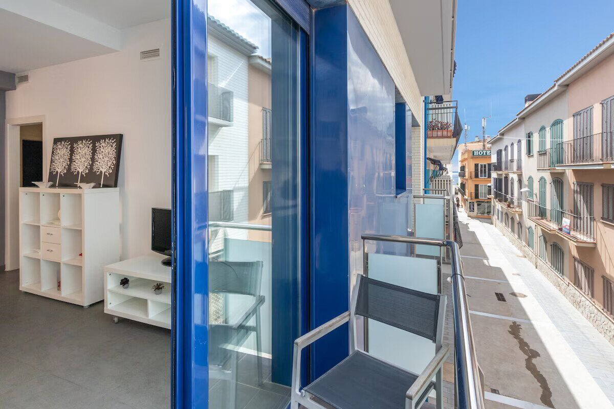 A balcony with a glass railing, a white entertainment unit, and a view of a street with buildings.