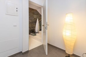 Ein Flur mit einer weißen Tür, einer Steinwand, einer Treppe und einer hohen, zylindrischen Stehlampe.